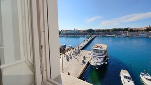 Vista desde una ventana sobre un puerto con barcos amarrados, un muelle y edificios al fondo.
