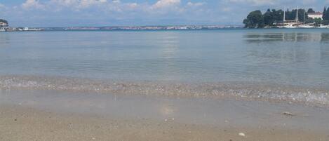 A beach with calm waters, a distant cityscape, and a few boats.