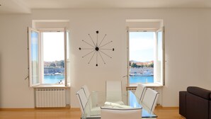 Un salón moderno con una mesa de comedor de cristal, sillas blancas y vistas a un puerto deportivo.
