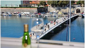 Un puente sobre el agua, con gente caminando, barcos amarrados y una botella de vino al frente.