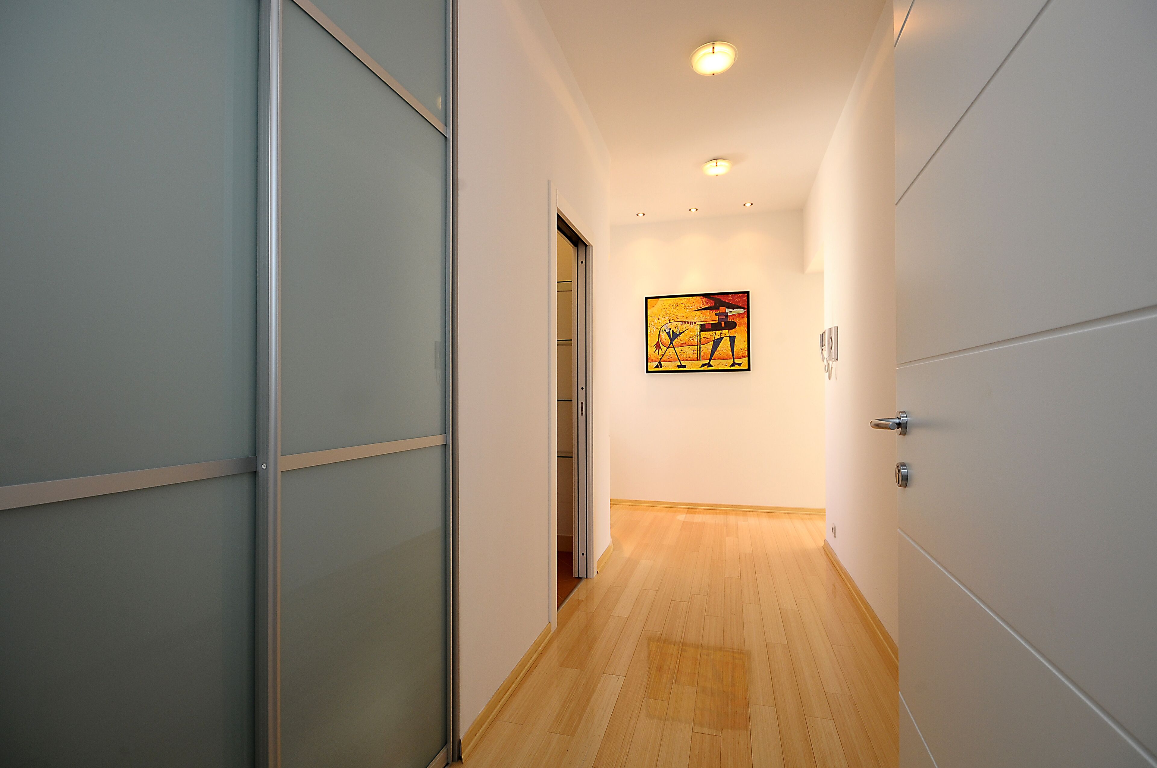 A hallway with a wooden floor, white walls, and a painting on the wall.