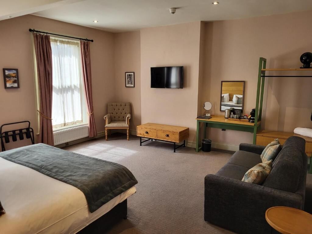 A hotel room with a bed, a sofa, a desk, a TV, a chair, and a window with curtains.