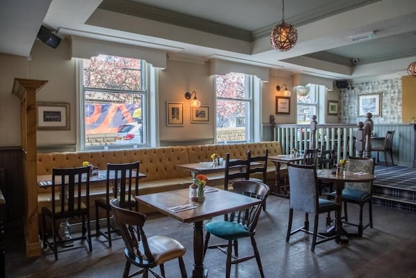 Un restaurant avec des tables et des chaises en bois, un banc rembourré et de grandes fenêtres donnant sur l’extérieur.