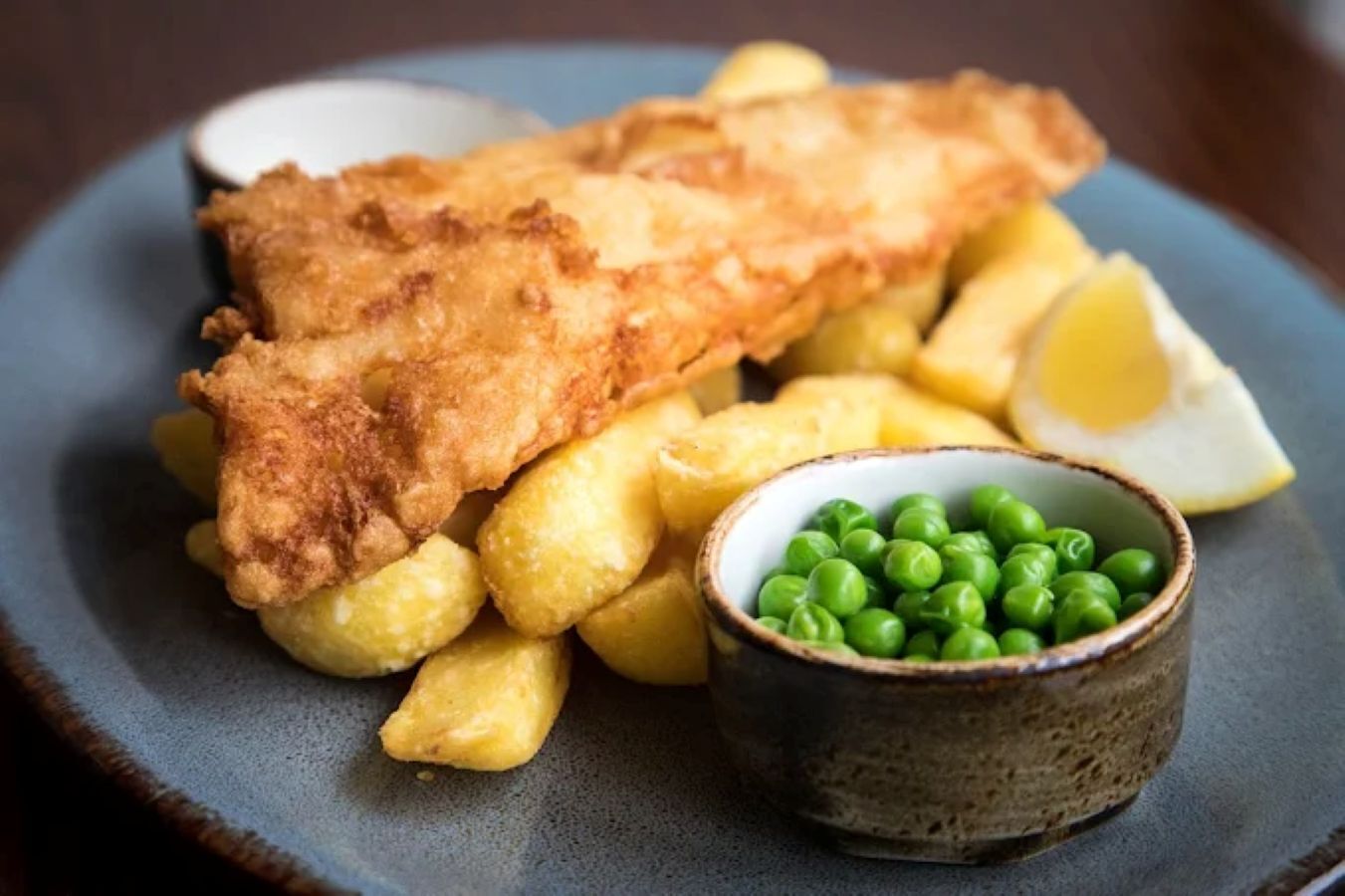 Un piatto di fish and chips con piselli e spicchio di limone.