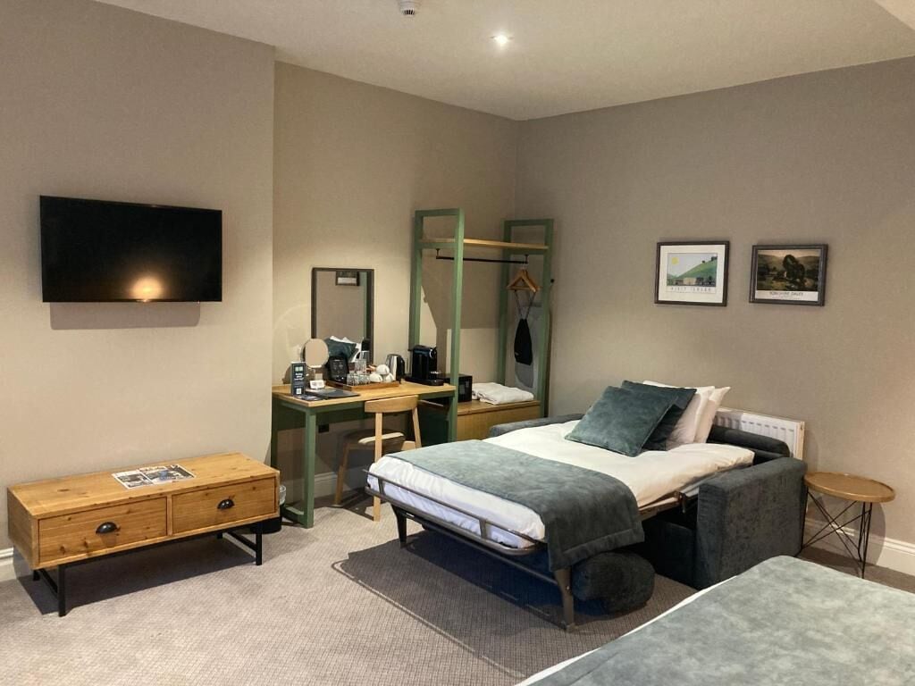 A modern hotel room with a bed, bedside table, desk, chair, and a TV mounted on the wall.