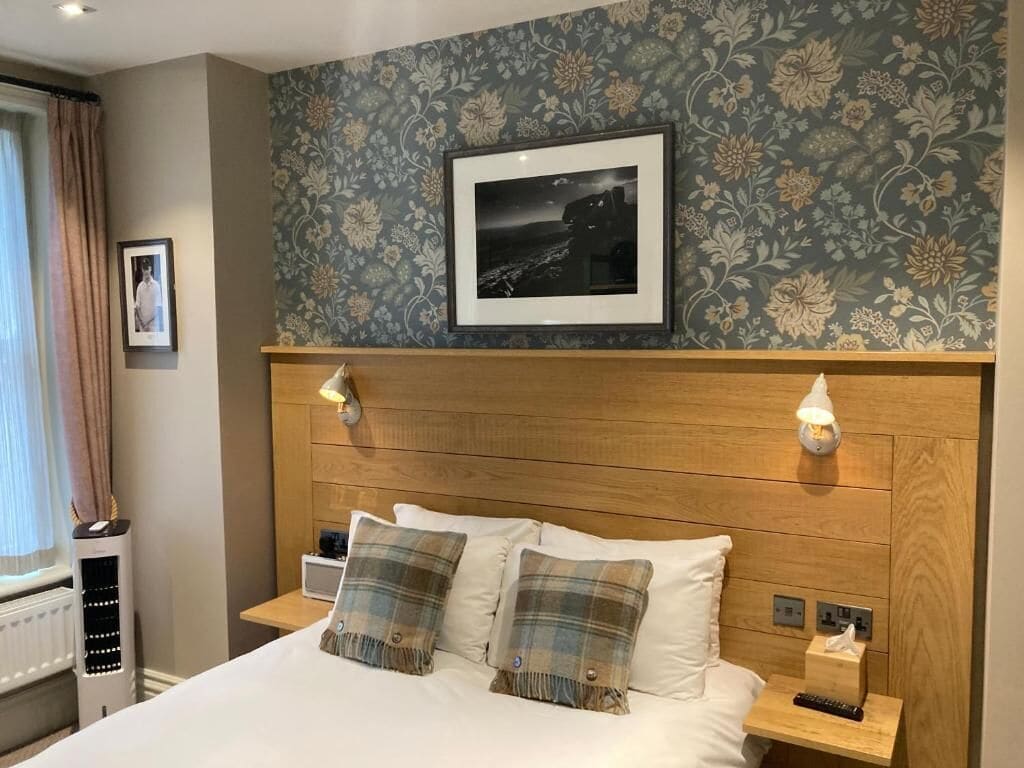 Une chambre d’hôtel avec un lit, deux tables de chevet, une commode, un tableau encadré au mur et une fenêtre avec des rideaux.