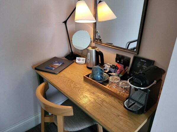 Un escritorio de madera con una computadora portátil, un espejo, una tetera, una bandeja con tazas y una cafetera.