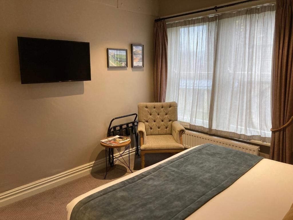 Een hotelkamer met een bed, een stoel, een tafeltje, een televisie en een raam met gordijnen.