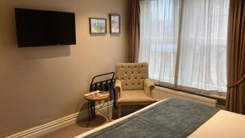 Een hotelkamer met een bed, een stoel, een tafeltje, een televisie en een raam met gordijnen.