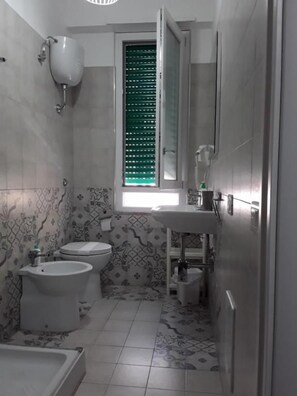 A bathroom with a toilet, bidet, sink, and a window with blinds. - B&b Le due Costiere (Salerno)