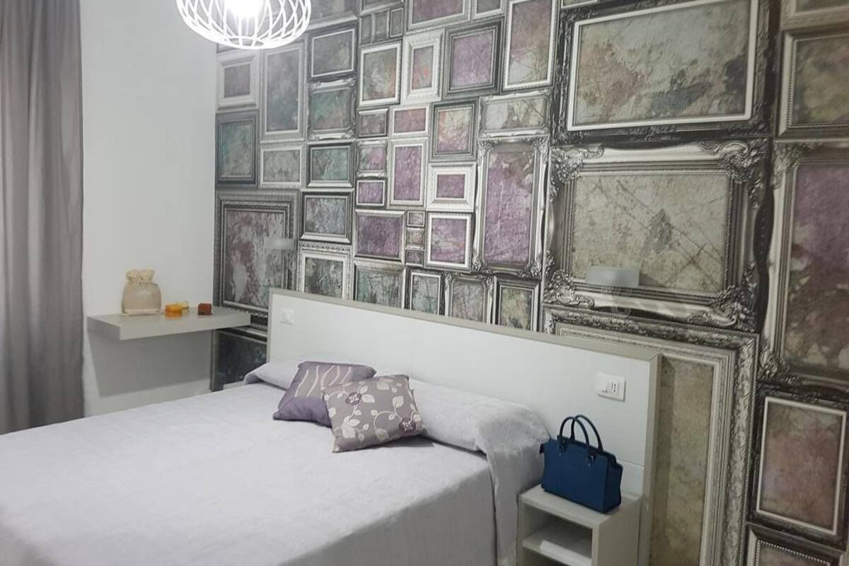A bedroom with a bed, a nightstand, a blue handbag, and a wall with a mosaic pattern.