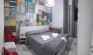 A hotel room with a bed, a red chair, a small table, and a wall with colorful patterns. - B&b Le due Costiere (Salerno)