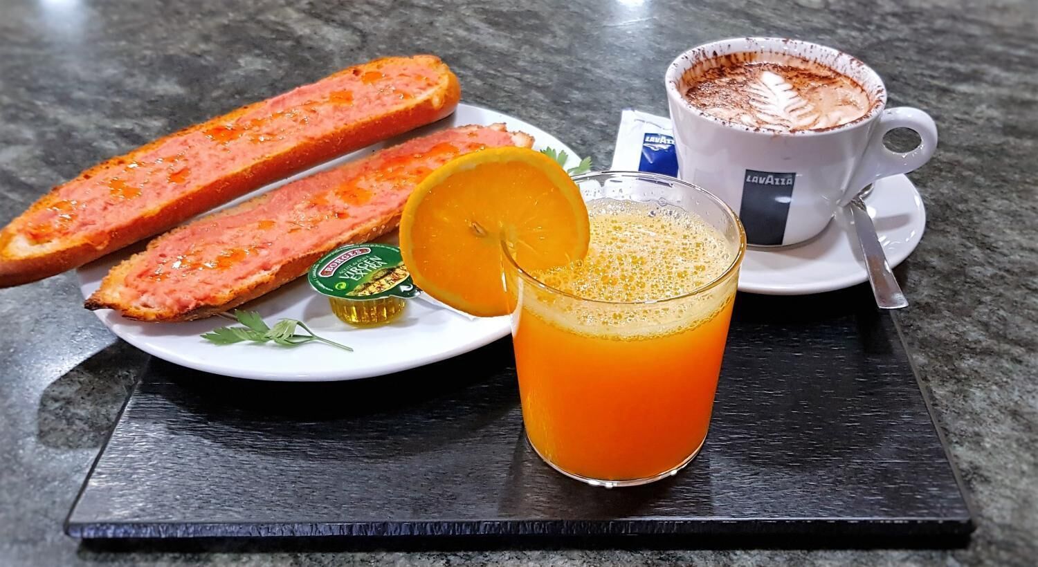 En tallrik med två brödskivor, ett glas apelsinjuice och en kopp kaffe på ett bord.