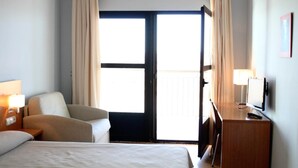 Habitación de hotel con cama, una silla, un escritorio, un televisor y un ventanal grande con cortinas.