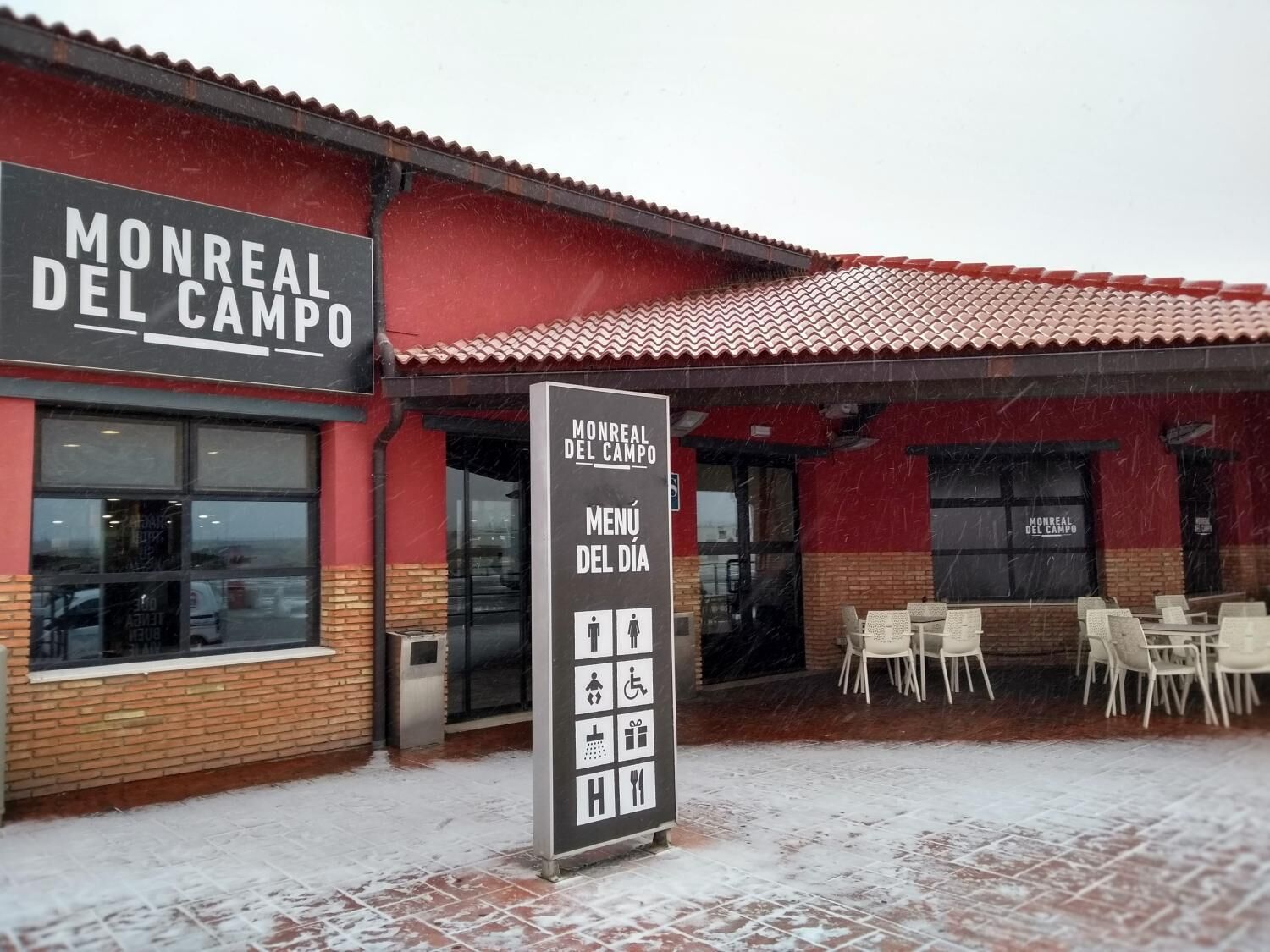 Un restaurante llamado 'Monreal del Campo' con un cartel que muestra los artículos del menú y símbolos que indican servicios como acceso para sillas de ruedas y una sala para bebés.