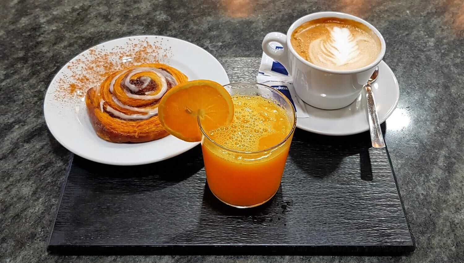 A breakfast setting with a plate of cinnamon rolls, a glass of orange juice, and a cup of coffee on a black tray.