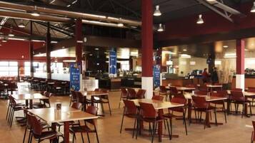 Una amplia cafetería con varias mesas y sillas, una zona de mostrador y un panel de menú visible.