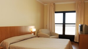 Una habitación de hotel con cama, una silla, televisor y ventana con cortinas.