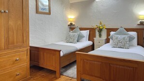 Une chambre à coucher avec deux lits en bois, une armoire en bois, un puits de lumière et une table de chevet avec une lampe et un vase de fleurs.