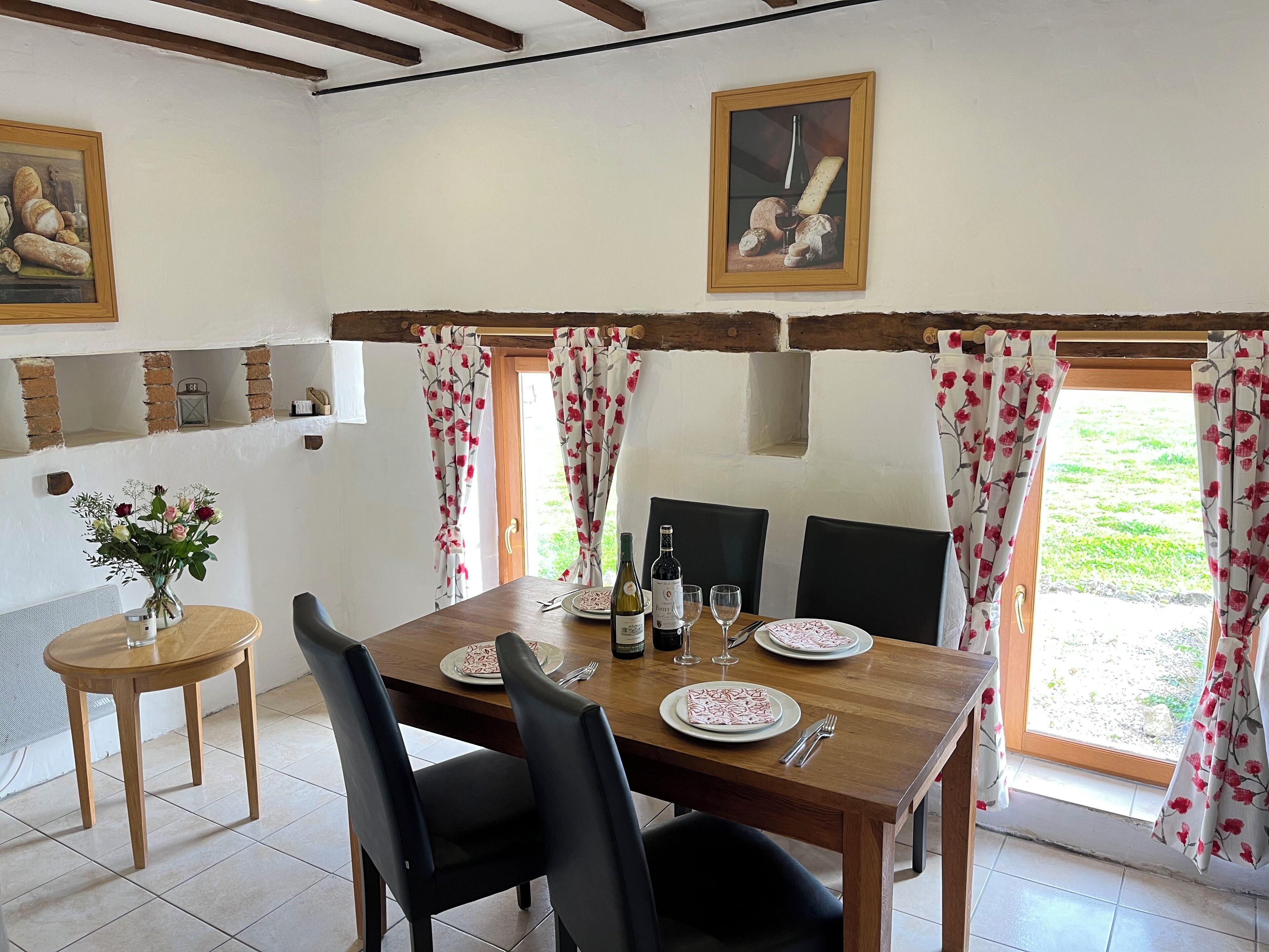 A dining area with a wooden table set for two, a vase of flowers, and a painting on the wall.