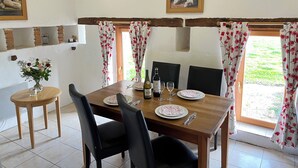 Un coin repas avec une table en bois dressée pour deux personnes, un vase de fleurs et un tableau accroché au mur.