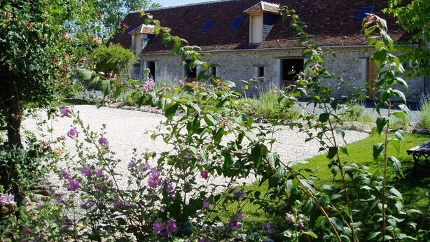A rustic stone building with a sloped roof, surrounded by lush greenery and flowering plants. - Le Pluvier - Luxury 3 bedroom holiday home with heated pool in the Loire Valley (Cussay)