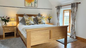 A bedroom with a wooden bed, a nightstand with a lamp, a vase with flowers, and a painting on the wall. - Le Pluvier - Luxury 3 bedroom holiday home with heated pool in the Loire Valley (Cussay)