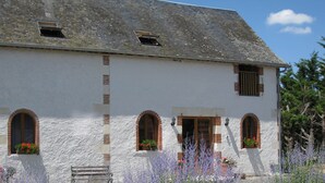 A white building with multiple arched windows and a door, surrounded by various plants and a bench. - Le Pluvier - Luxury 3 bedroom holiday home with heated pool in the Loire Valley (Cussay)