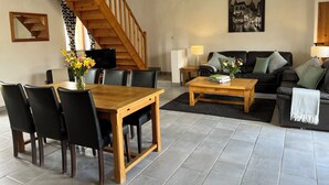 A spacious living room with a wooden dining table, black chairs, a sofa, and a staircase. - Le Pluvier - Luxury 3 bedroom holiday home with heated pool in the Loire Valley (Cussay)