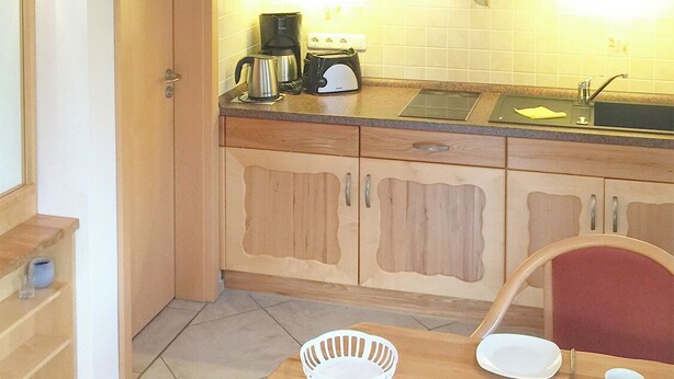 Een kleine keuken met houten kastjes, een spoelbak en een eethoek met een tafel gedekt voor twee personen.