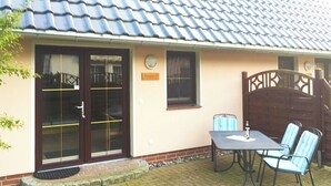Een gebouw met een pannendak, een glazen deur met metalen hendel, een kleine tafel met stoelen en een houten poort.