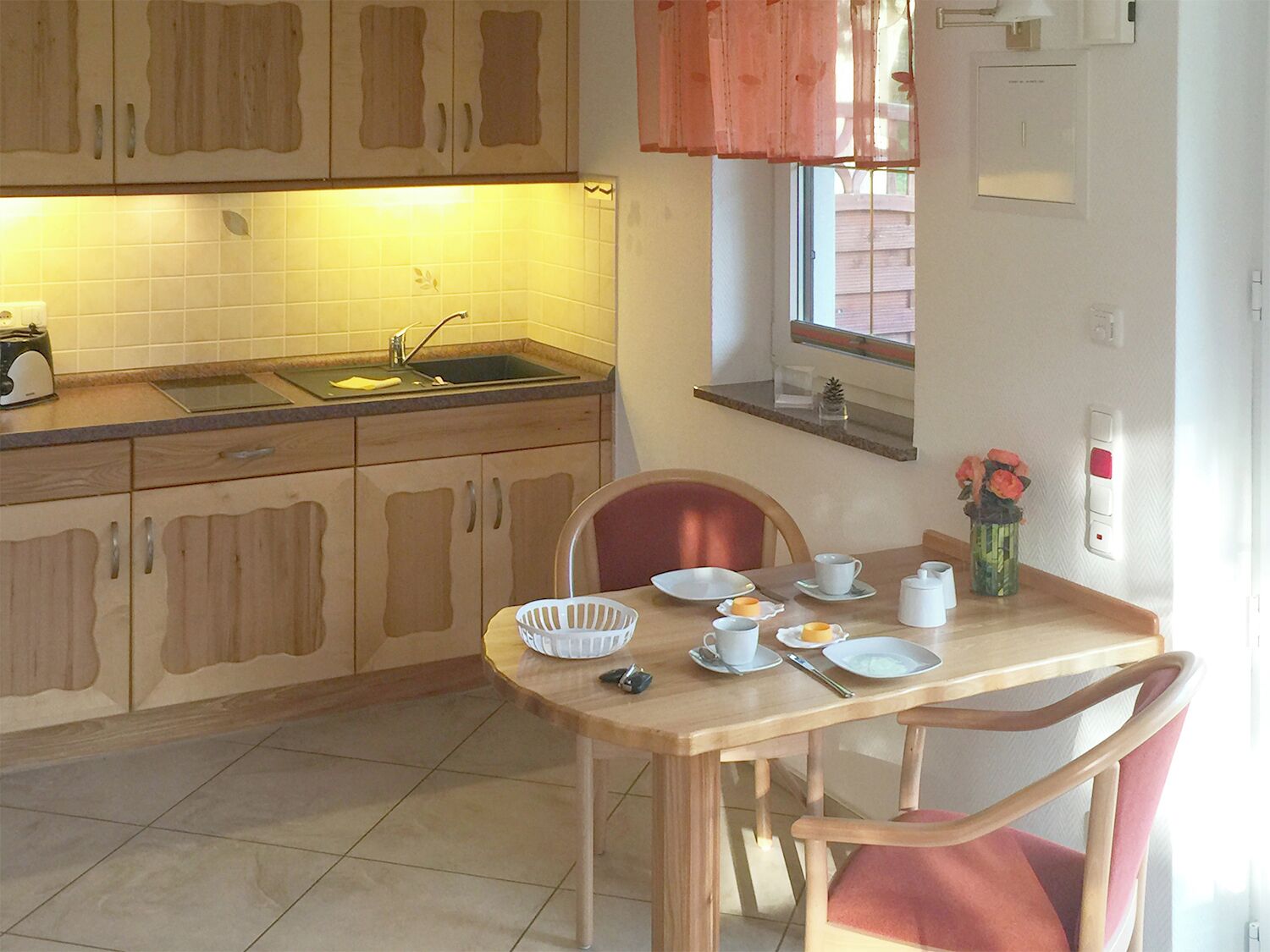 Una pequeña cocina con un lavamanos, un tostador y una mesa de comedor con sillas.