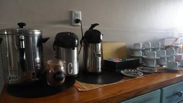 Uma cozinha compacta com cafeteira, chaleira, um pote e uma pilha de xícaras e pires.