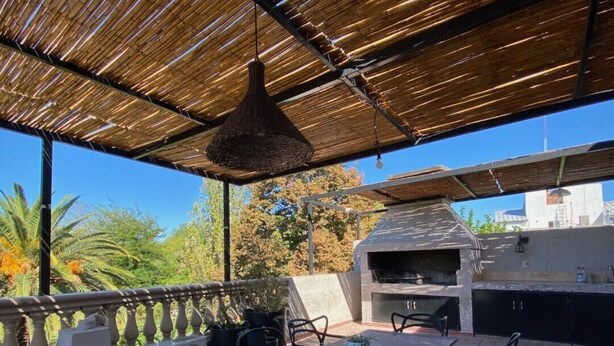 An outdoor patio with a long table and chairs, a grill, and potted plants. - Hotel Sienna (Mendoza)