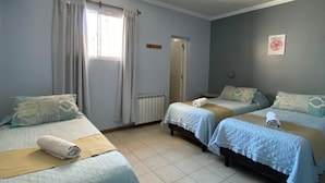Une pièce avec trois lits, un radiateur, une fenêtre avec des rideaux et une porte.