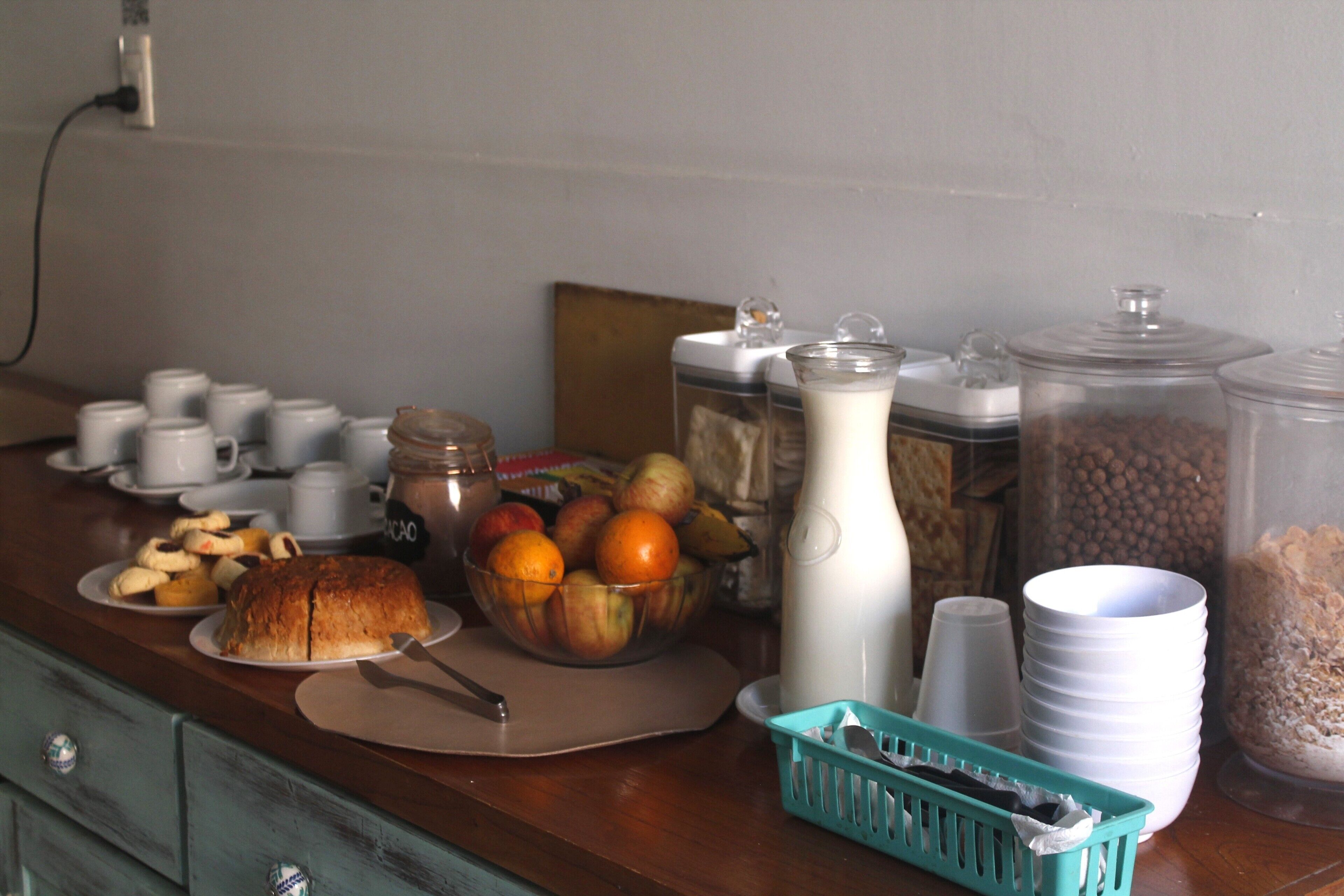 Buffet de café da manhã com diversos alimentos, incluindo um pão, uma tigela de frutas e vários recipientes com condimentos.