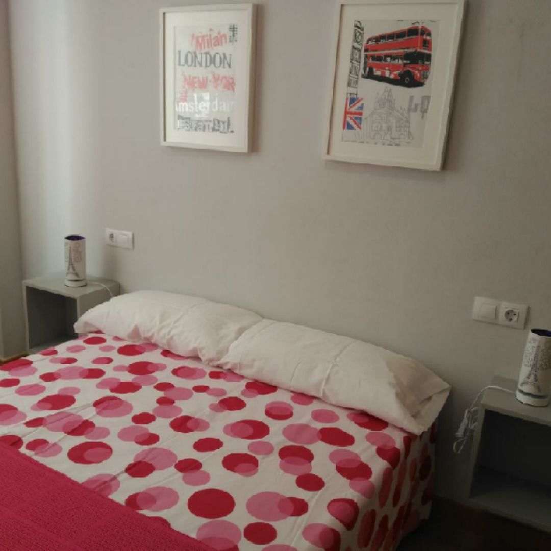 Un dormitorio con una cama, almohadas, una mesita de noche y dos cuadros en la pared.