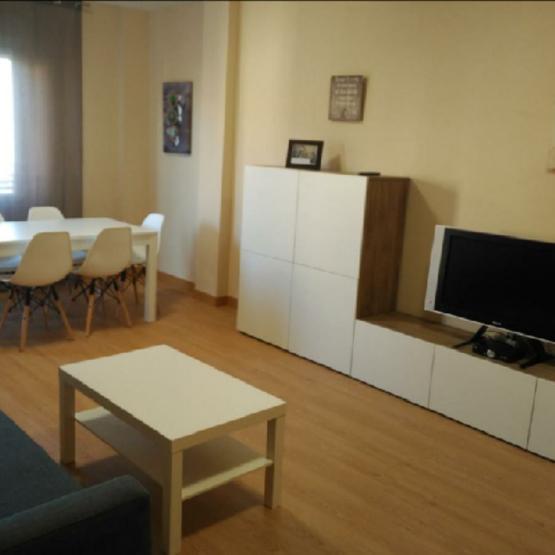 Una sala de estar con un sofá, una mesa de centro, un televisor y un comedor con sillas y una mesa.