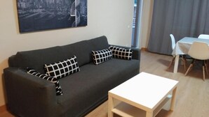 A living room with a dark grey sofa, two patterned pillows, a white coffee table, and a cityscape painting on the wall. - Zamora Apartments (Zamora)
