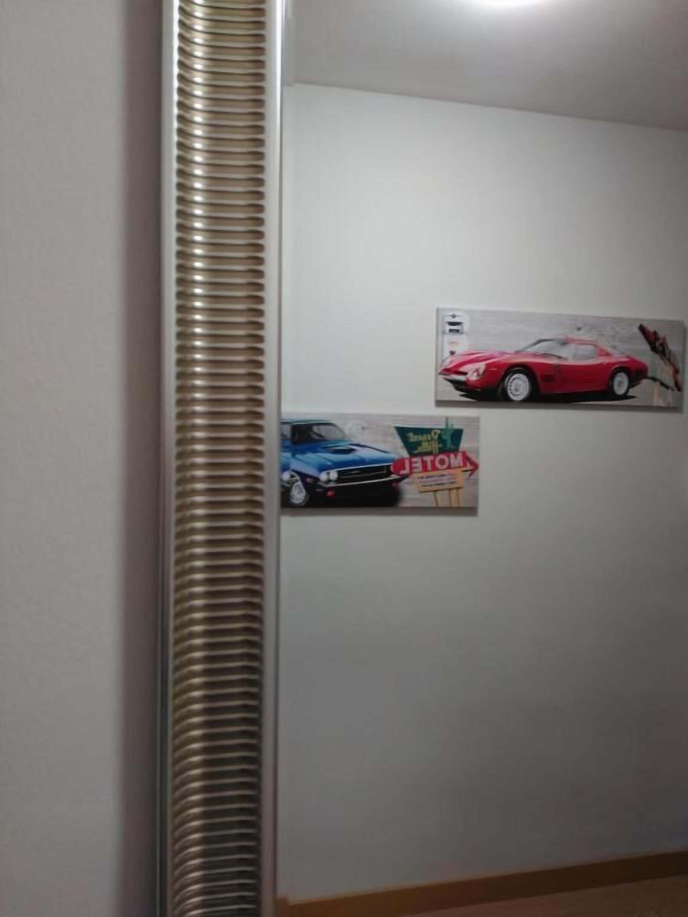 Et værelse med en hvid væg, en radiator og to billeder af biler i rammer.
