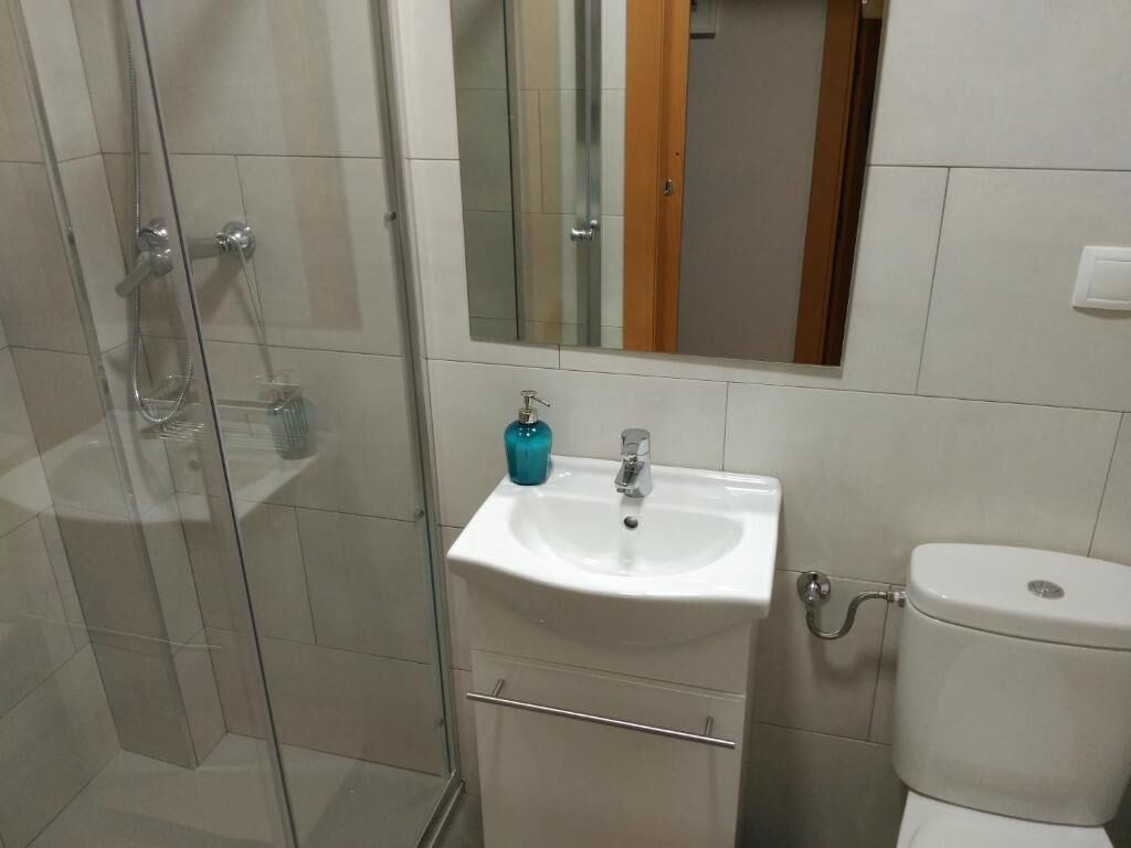 Un baño con cabina de ducha de vidrio, un lavamanos blanco con un espejo encima y un inodoro.
