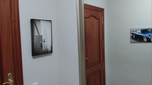 A hallway with a wooden door, a framed picture of a cityscape, and a framed picture of a car. - Zamora Apartments (Zamora)