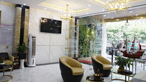 A modern lobby with marble flooring, two leather armchairs, a large flat-screen TV, a ceiling chandelier, and a glass wall with a green plant backdrop. - Anh Nguyet Hotel Da Nang (Da Nang)