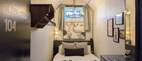 Una habitación de hotel con cama, escritorio, espejo y ventana con cortinas.