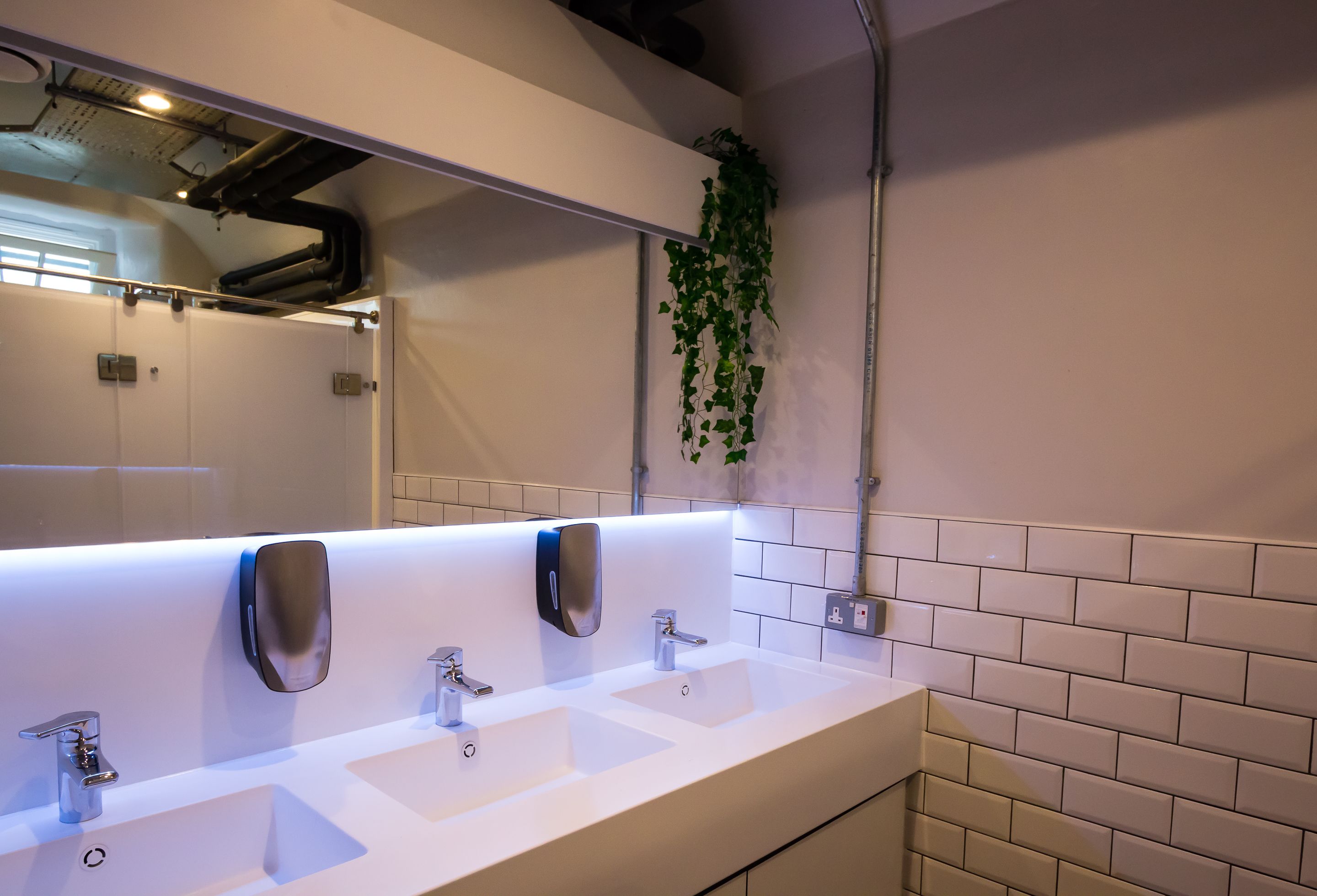 A modern bathroom with three sinks, a large mirror, and a wall-mounted plant.