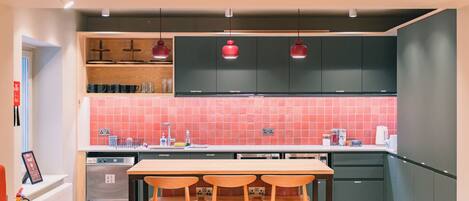 A modern kitchen with a dining area, equipped with a dishwasher, oven, and a red tiled backsplash.