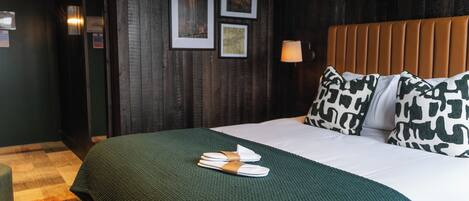 A hotel room with a bed, pillows, a lamp, and a green blanket.