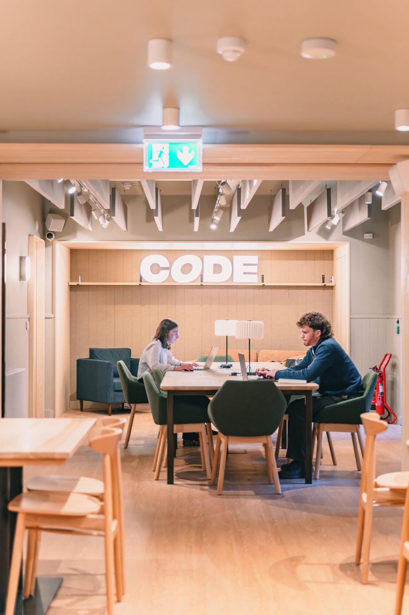 A modern workspace with a 'CODE' sign, wooden furniture, and overhead lighting.