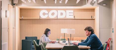 A modern workspace with a 'CODE' sign, wooden furniture, and overhead lighting.