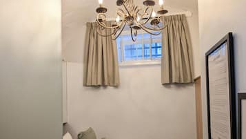 Habitación de hotel con cama, almohadas, una araña, cortinas, ventana y cartel de bienvenida.